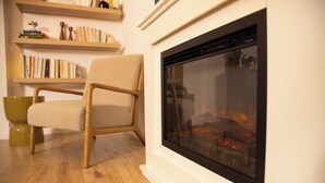A modern living room with a fireplace, wooden flooring, a beige armchair, and a bookshelf. - Cozy apartment with garden near Cologne (Frechen)