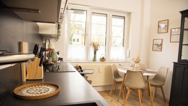 A kitchen with a dining area, a window with curtains, and a radiator. - Cozy apartment with garden near Cologne (Frechen)