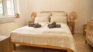 A bedroom with a wooden bed, white bedding, two bedside lamps, a window with a plant, and a crib. - Cozy apartment with garden near Cologne (Frechen)