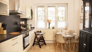 A kitchen with a dining area, featuring a stove, oven, cabinets, and a window with a view. - Cozy apartment with garden near Cologne (Frechen)