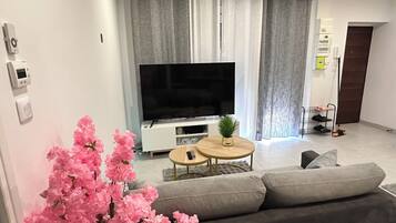 Una sala moderna con televisor de pantalla plana, sofá gris y una pequeña mesa redonda con una planta.