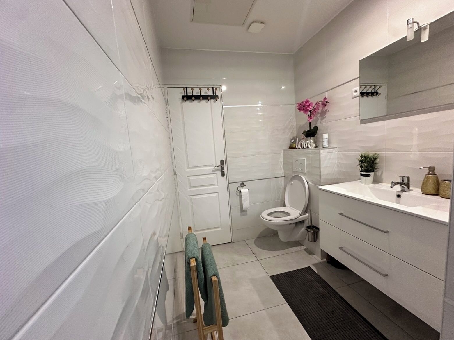 A modern bathroom with a toilet, sink, and mirror. There are towels hanging on a rack and a small plant on the counter.