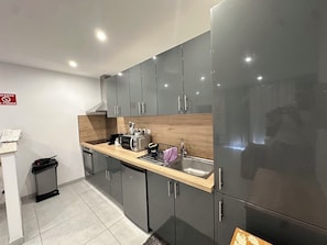 A modern kitchen with grey cabinets, a wooden countertop, a sink, and a stainless steel refrigerator.