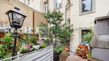 A courtyard with a variety of potted plants, a wooden bench, and a metal lamp post.
