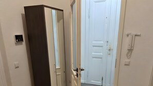 A room with a wooden floor, a round rug, a wardrobe, and a door leading to another room.