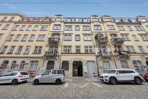 Ein mehrstöckiges Gebäude mit Balkonreihe, Hauseingang im Erdgeschoss und parkenden Autos.