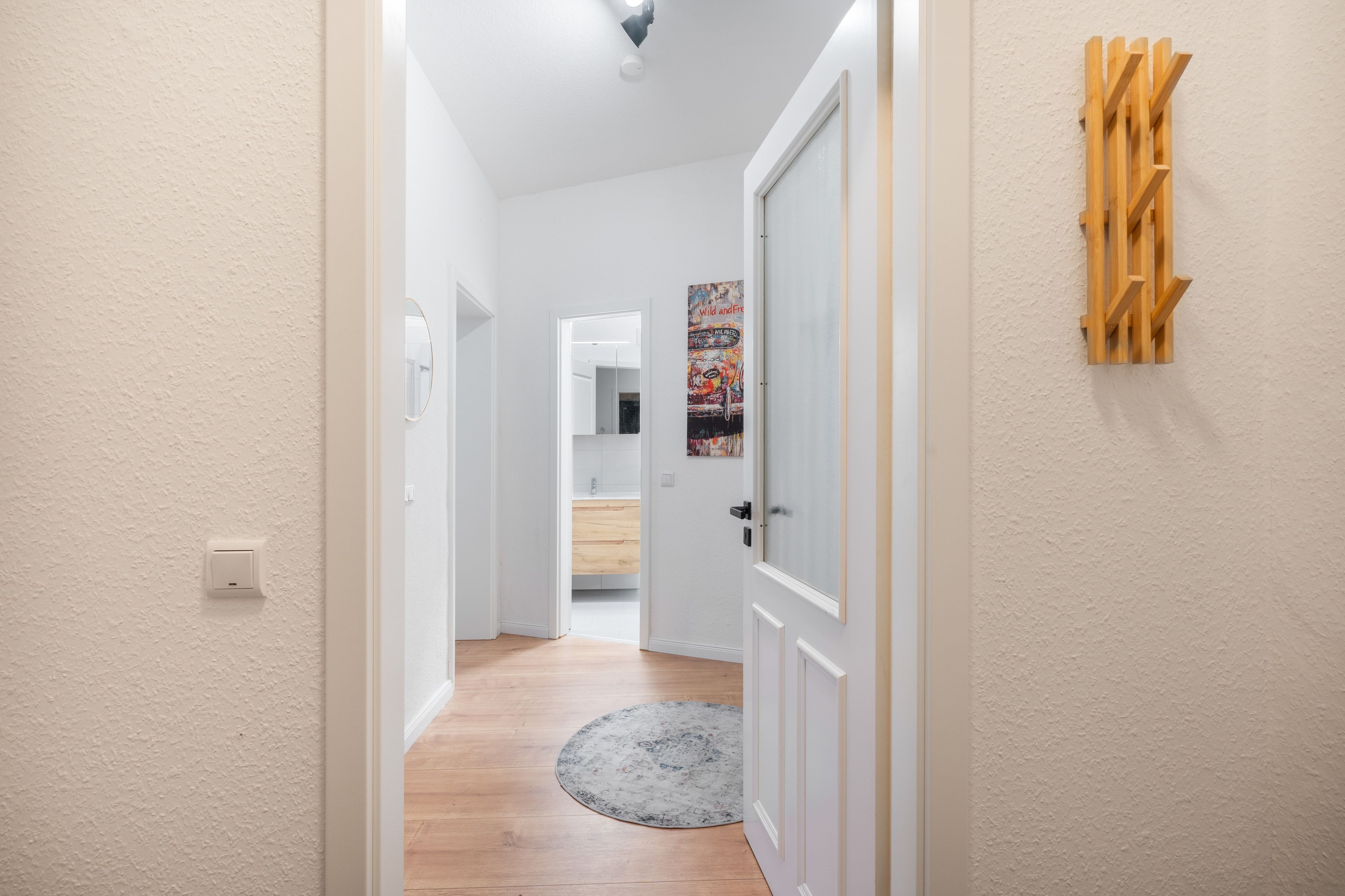 A hallway with a wooden floor, a round rug, and a door with a white frame.