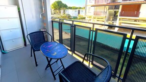 A balcony with two chairs, a small table, and a view of a swimming pool and buildings. - Charming Family Flat Near the Beach (San Michele al Tagliamento)