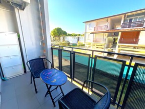 A balcony with two chairs, a small table, and a view of a swimming pool and buildings. - Charming Family Flat Near the Beach (San Michele al Tagliamento)