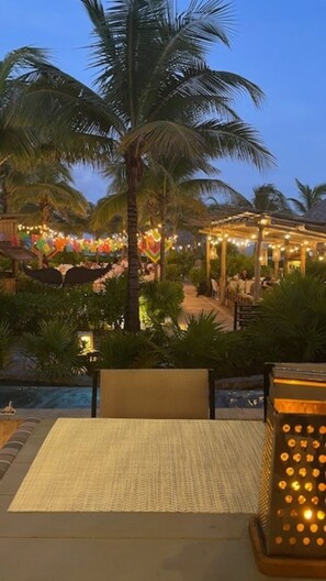 Ein tropisches Resort mit Poolbereich, Palmen und einer überdachten Sitzgelegenheit mit Lichterketten.
