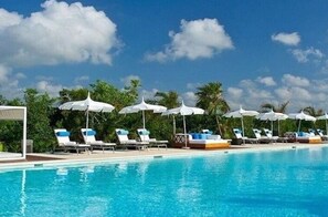 A poolside area with lounge chairs and umbrellas, surrounded by palm trees and a clear sky. - Vidanta riviera maya  2BR 3 bath need to check availability before booking (Mayan Palace)