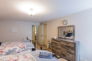 A bedroom with two beds, a dresser, a clock, and a door leading to another room.