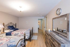 A bedroom with a bed, dresser, mirror, and a hallway leading to another room. - Rosa's Sea View Serenity Stays (Stratford)