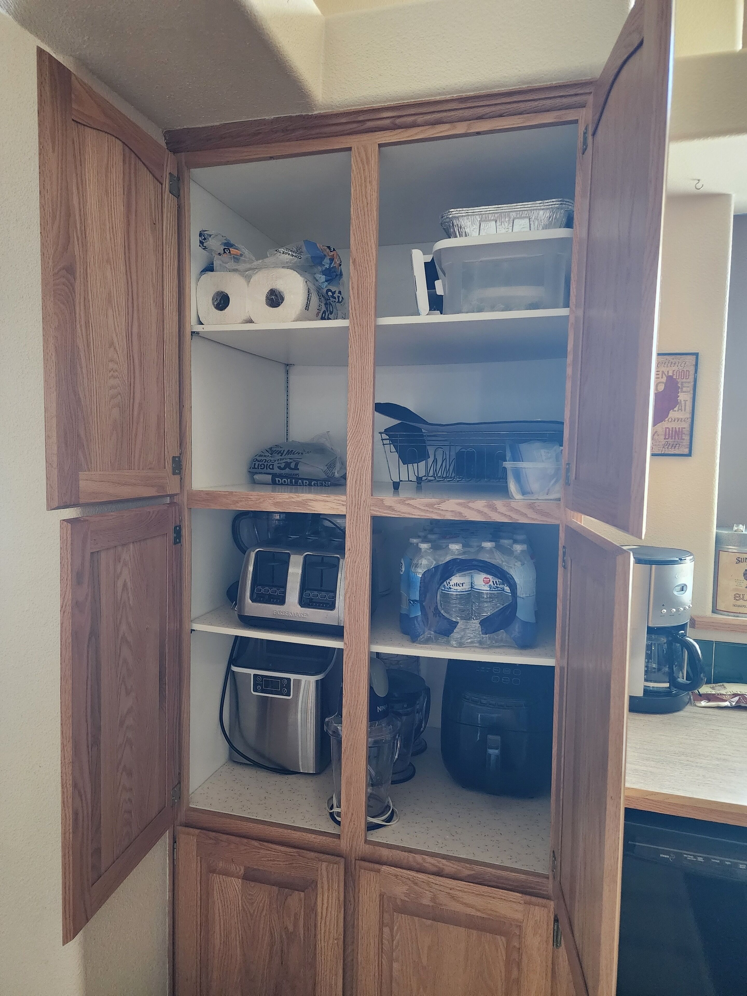 A wooden cabinet with multiple shelves containing kitchen appliances, storage containers, and a coffee maker.