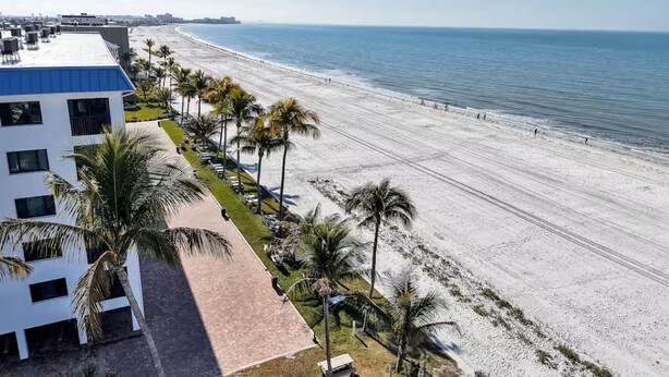 Ein Hotel direkt am Strand mit freiem Blick auf den Ozean, Palmen und einem befestigten Weg zum Strand.