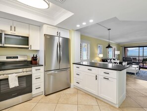 A modern kitchen with stainless steel appliances, white cabinetry, and a large island. - Seaside Resort 201: Stunning Beachfront, heated pool (Fort Myers Beach)