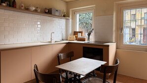 Una cocina con azulejos blancos tipo metro, una ventana con vistas, una mesa con sillas y un estante con botellas.