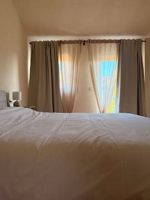 A hotel room with a bed, curtains, a nightstand, and a lamp. - Kiki's - A spacious house with a garden in the Langhe. (Castagnole delle Lanze)