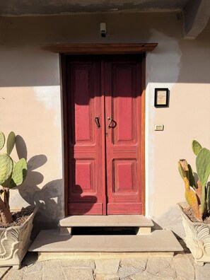 Uma porta dupla vermelha com uma pequena placa acima, embutida em um edifício com base de pedra e parede revestida em estuque.