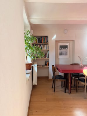 Uma área de refeições com uma mesa vermelha, cadeiras, uma estante e um radiador.