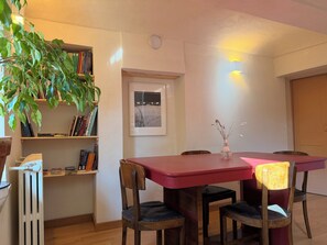 A dining area with a red table, wooden chairs, a bookshelf with books, a framed picture on the wall, and a radiator. - Kiki's - A spacious house with a garden in the Langhe. (Castagnole delle Lanze)