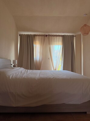 A bedroom with a bed, curtains, a lamp, and a window with daylight. - Kiki's - A spacious house with a garden in the Langhe. (Castagnole delle Lanze)