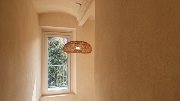 Un pasillo estrecho con una ventana, una lámpara de fibra y una puerta blanca.