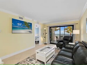 Ein Wohnzimmer mit einer Couch, einem Couchtisch, einem Strandbild und Blick durch eine Glastür nach draußen.