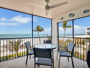 Een balkon met uitzicht op het strand, een ronde tafel met stoelen en een plafondventilator.