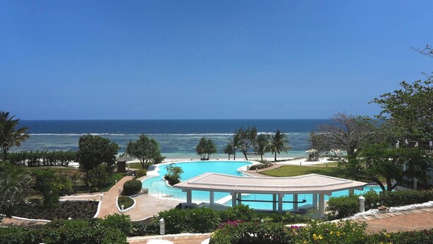 A resort with a pool, palm trees, and a view of the ocean.