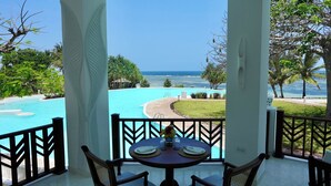 A balcony with a table set for dining, overlooking a pool and the ocean.