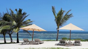A beach with lounge chairs and umbrellas, palm trees, and a view of the ocean.