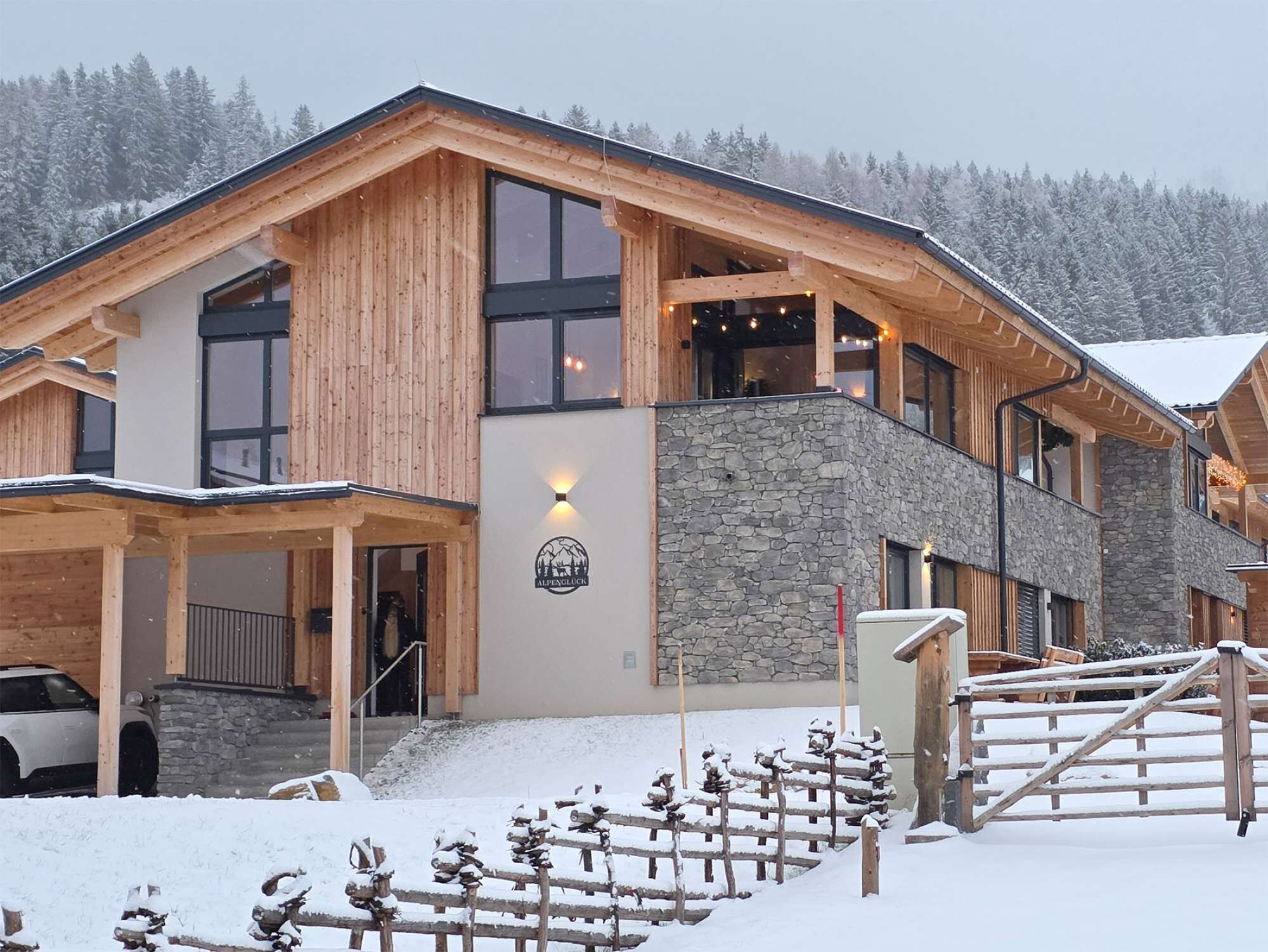 Un bâtiment en bois avec une façade en pierre, de grandes fenêtres et une enseigne sur laquelle on peut lire « Alpenglück ».