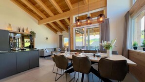 Une cuisine moderne avec un coin repas, des poutres apparentes en bois au plafond et de grandes fenêtres.