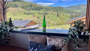 Une vue depuis un balcon, avec une bouteille de vin, un verre et un coussin orné de la phrase « Qu'il neige ».