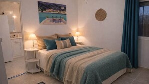 Une chambre à coucher comprenant un lit, deux tables de chevet, un tableau, une décoration murale en fibres tressées et une vue sur l’extérieur.
