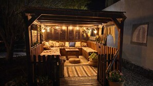 Un espace extérieur accueillant, aménagé avec un banc en bois, des coussins et des plantes en pot.