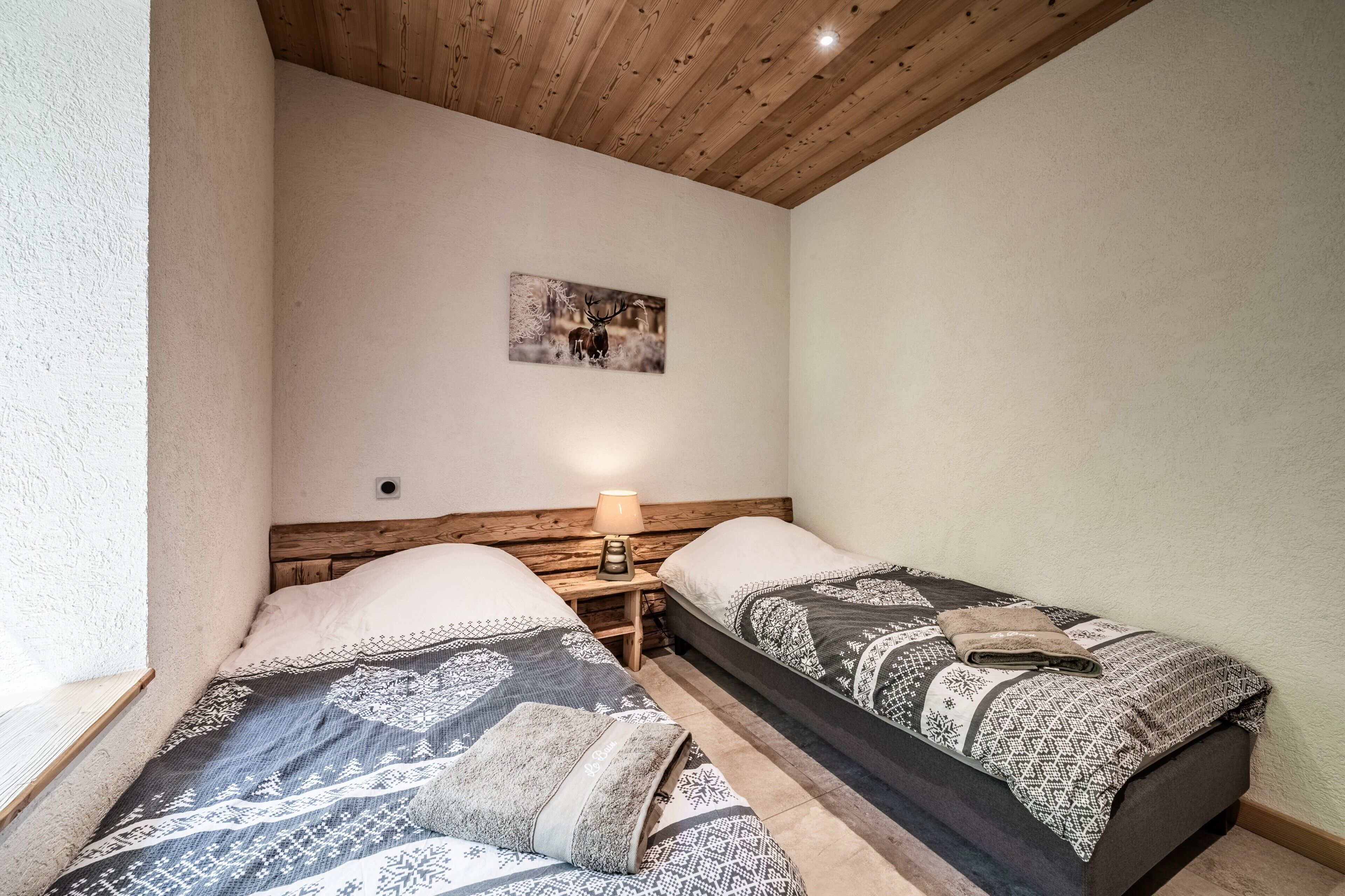 Un dormitorio con dos camas, techo de madera, un cuadro en la pared y una mesita de noche con lámpara.