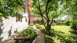 Un jardín con un camino, un árbol y un edificio con techo inclinado.