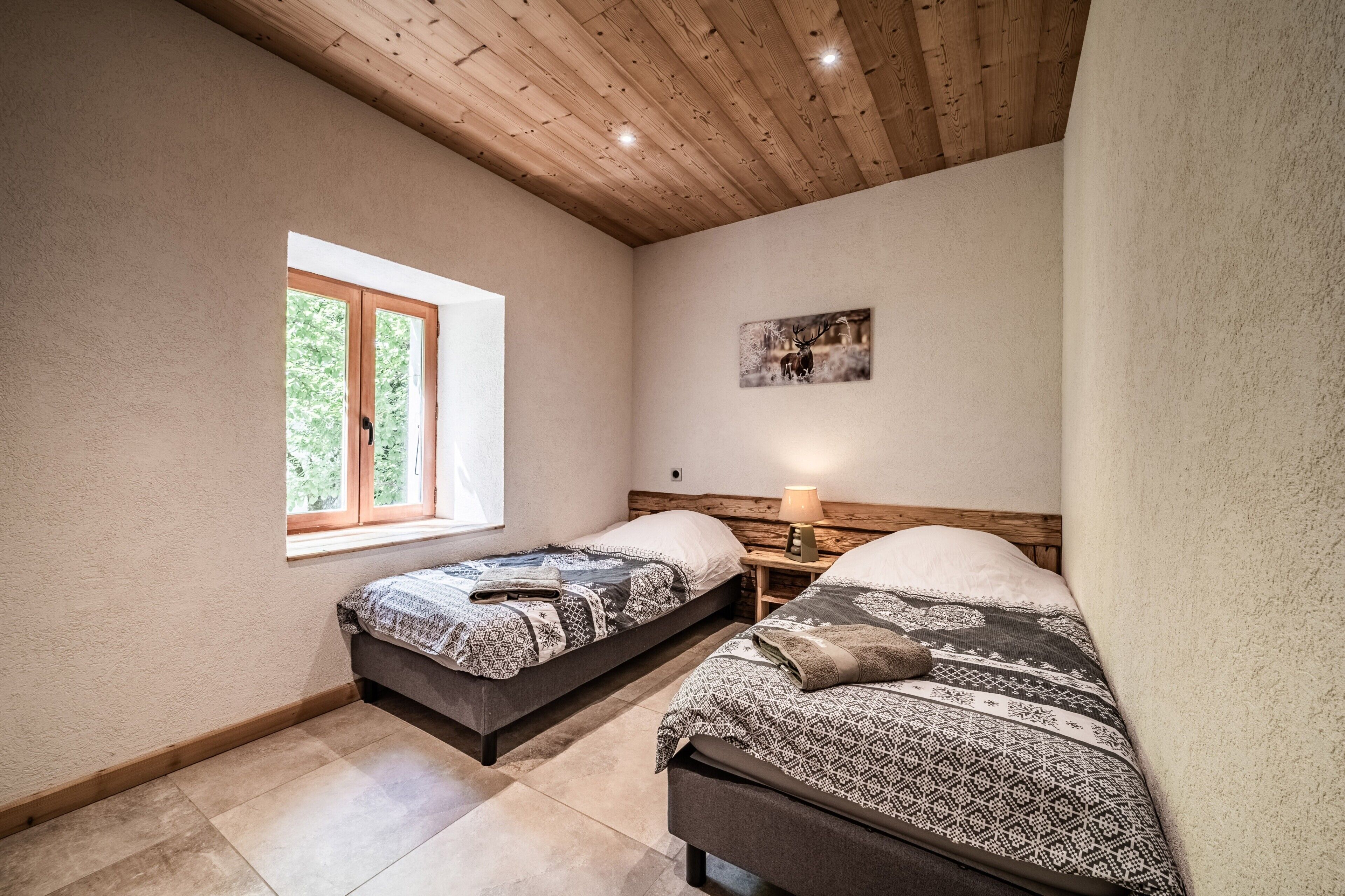 Een slaapkamer met twee bedden, een raam, een houten plafond en een aan de muur bevestigd schilderij.
