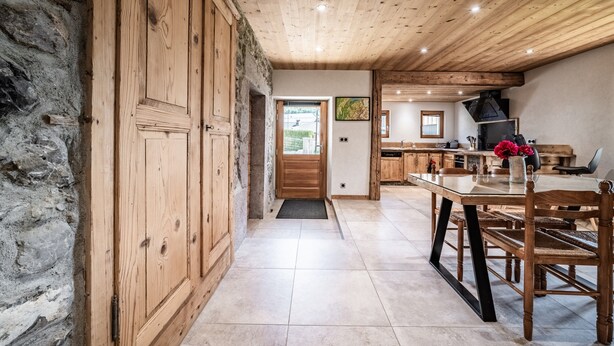 Un interior rústico con techos de madera, paredes de piedra, una zona de comedor con mesa y sillas, y una cocina visible al fondo.