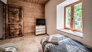 Un dormitorio con techo de madera, un televisor sobre una cómoda, una ventana con vistas y una colcha estampada.