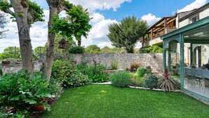 Un jardin bien entretenu, avec un mur de pierre, diverses plantes et un ciel d’un bleu éclatant.