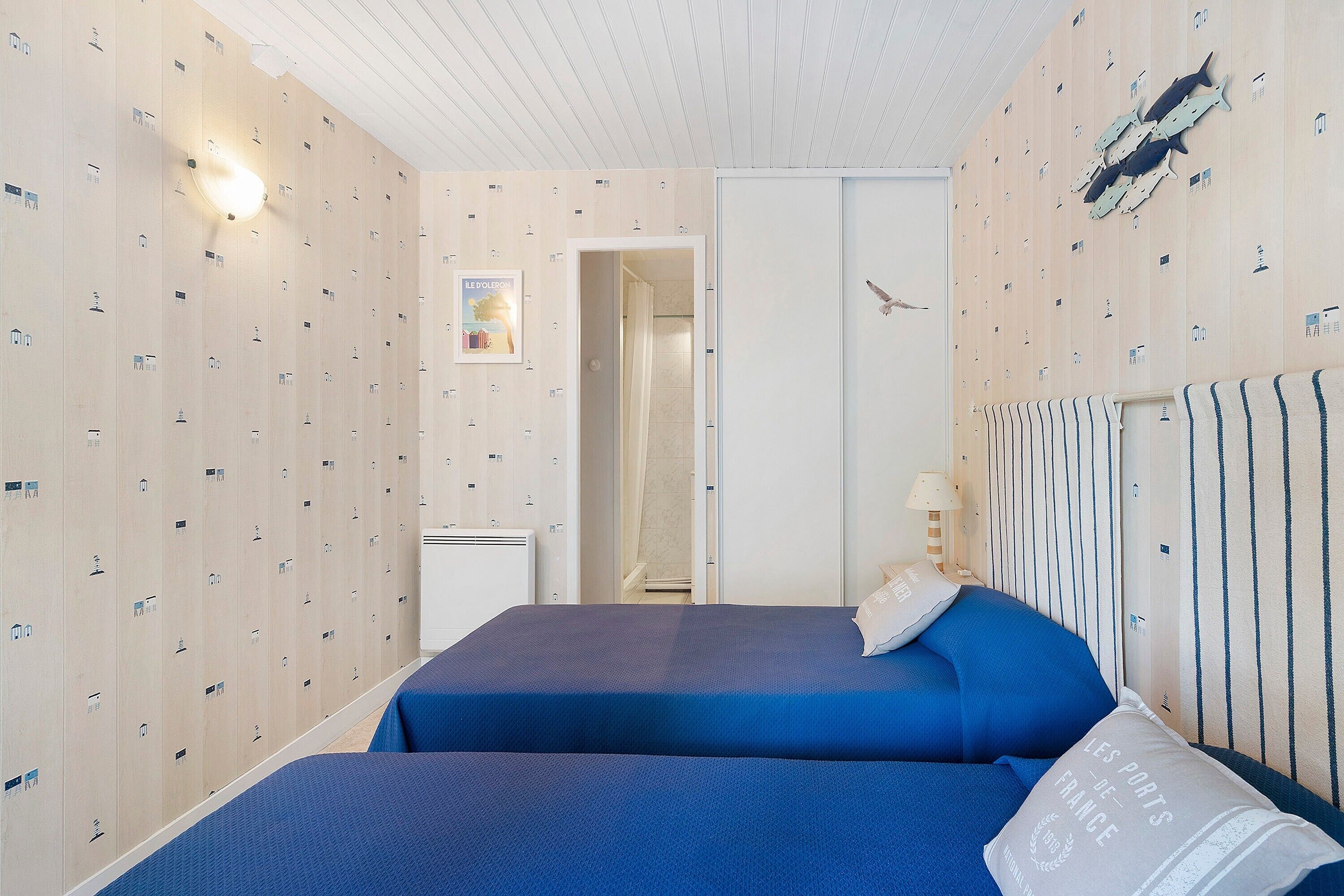Een hotelkamer met twee bedden, een douchegedeelte en een muur met nautische decoraties.