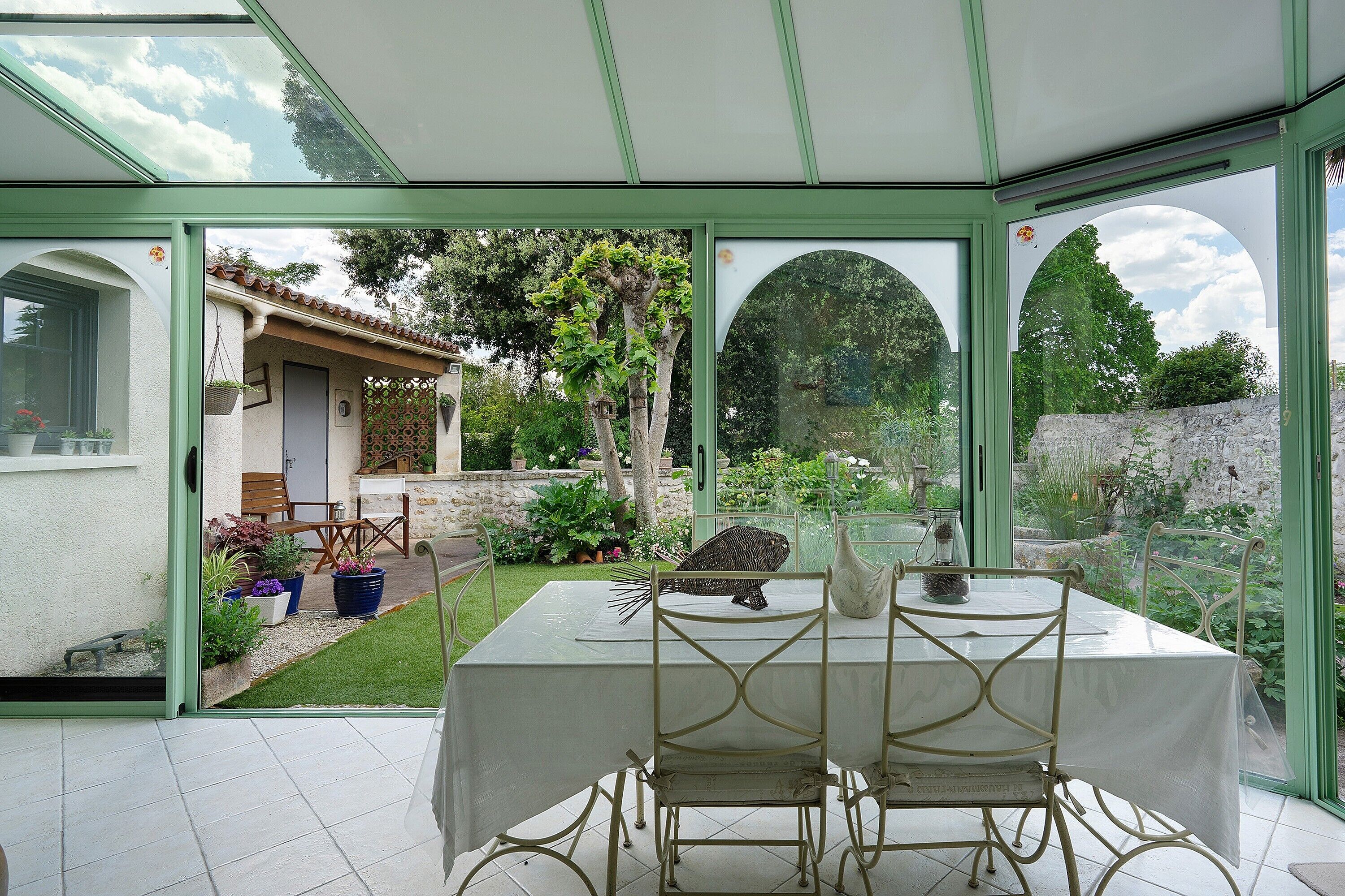 Een oranjerie met een tafel en stoelen, uitzicht op een tuin, en een deur naar een terras.