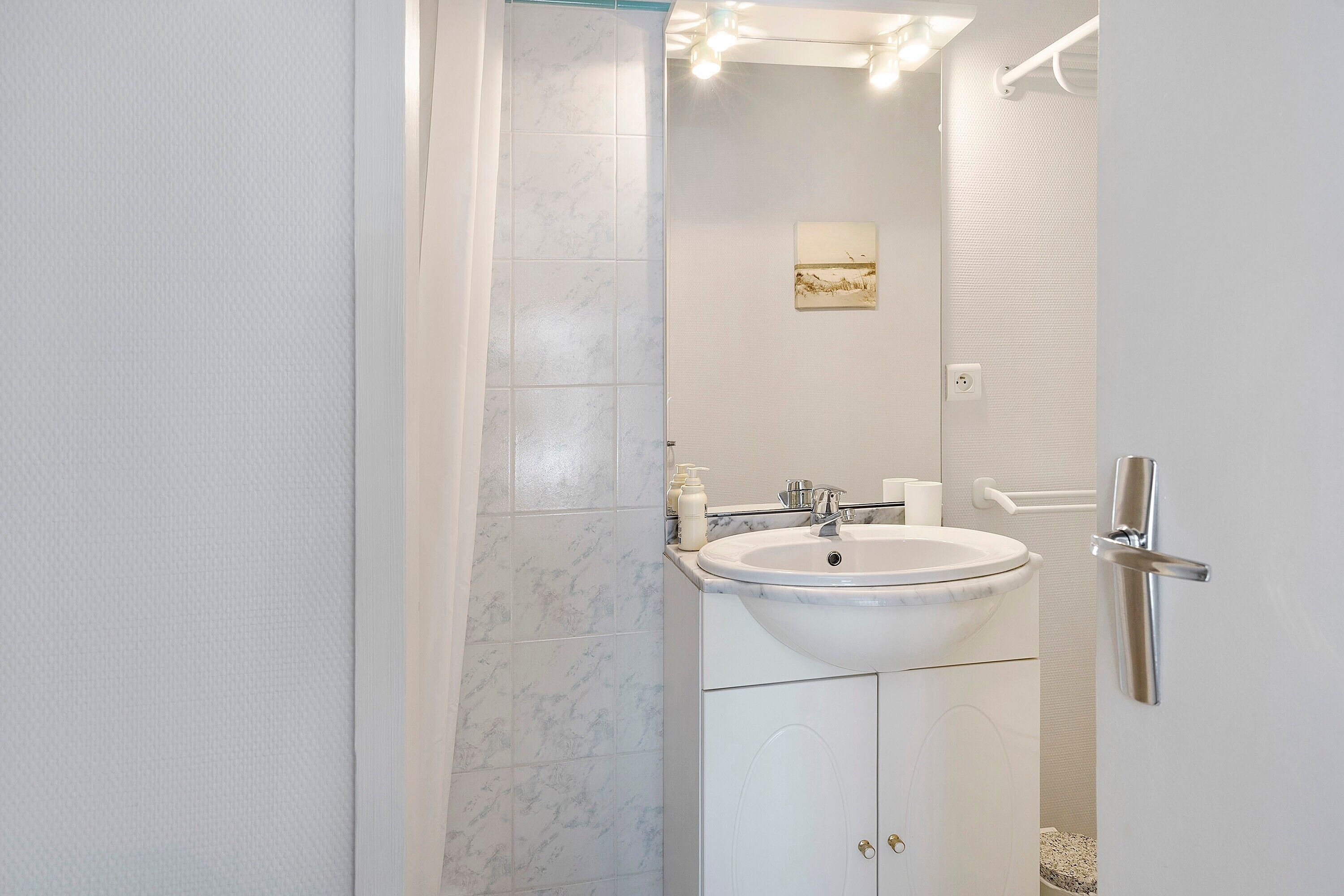 A bathroom with a white sink, mirror, and a door with a silver handle.