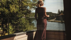 Une personne se tient sur une terrasse en bois, d’où l’on peut admirer des arbres et une étendue d’eau.