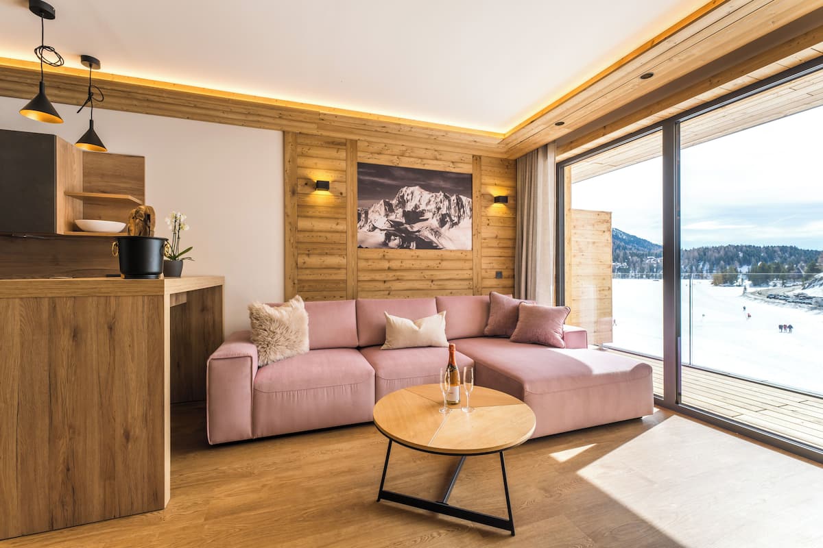 A modern living room with a wooden floor, a pink sofa, a round coffee table, and a large window with a mountain view.
