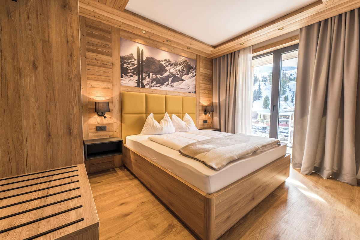A wooden-paneled bedroom with a bed, bedside lamps, and a view of a snowy landscape.