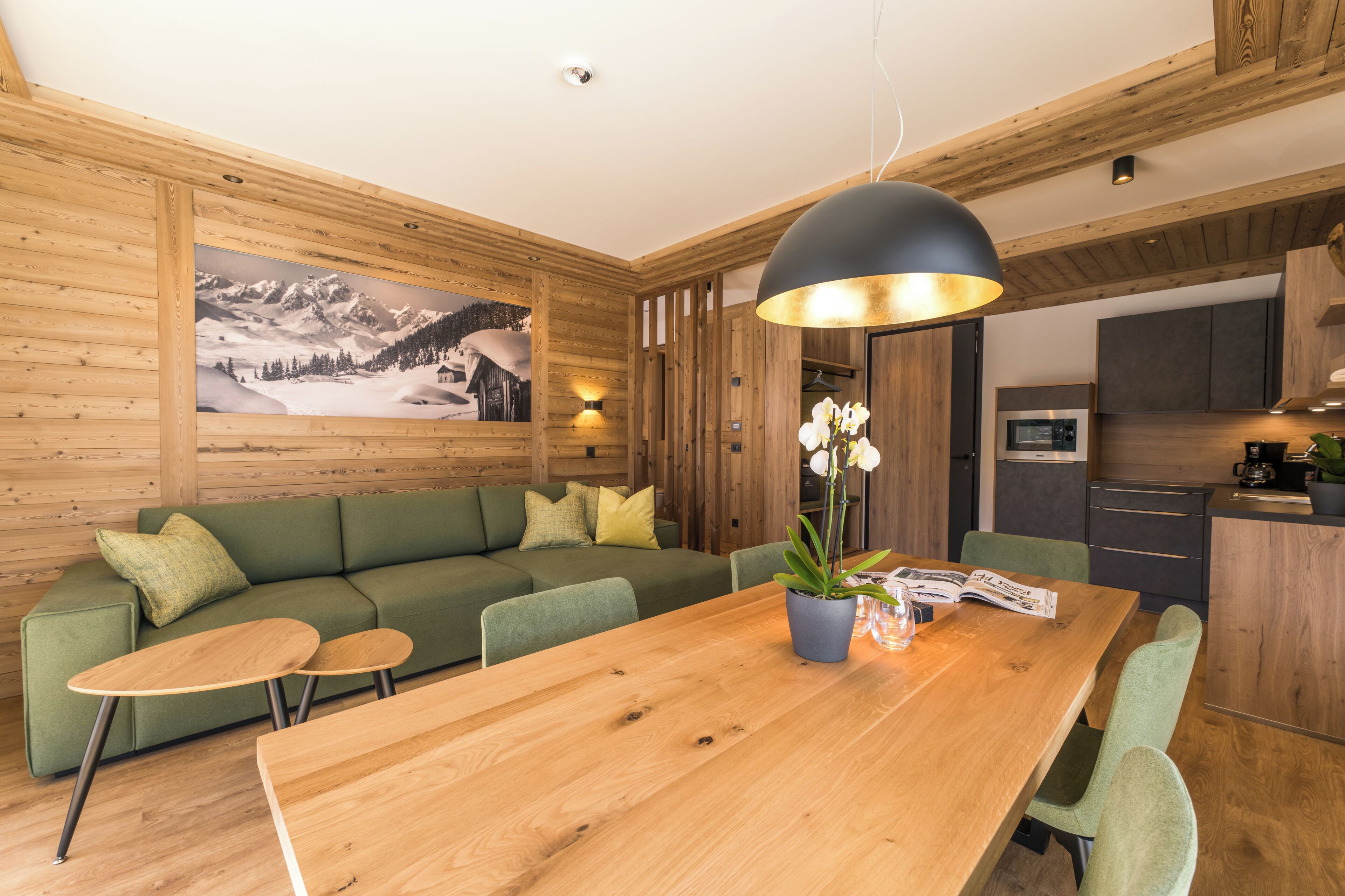 Un intérieur moderne avec une table à manger en bois, un canapé vert et un coin cuisine.